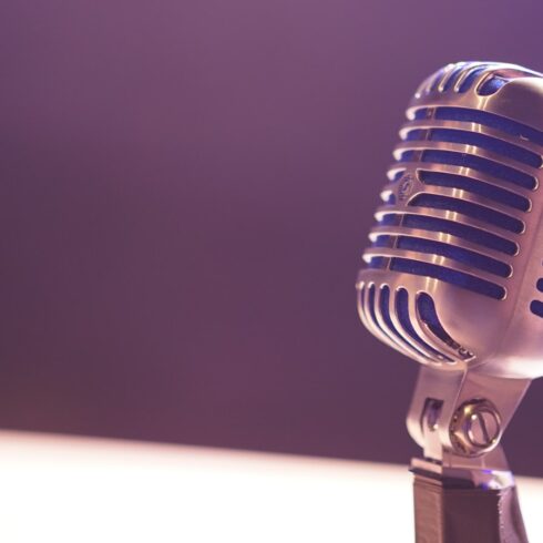 A vintage silver microphone with blue accents against a soft purple background